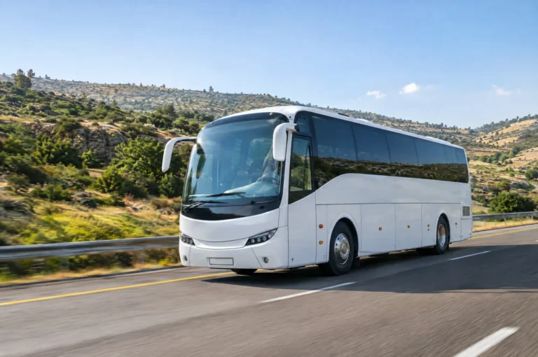 אוטובוס תיירים לבן בנסיעה בכביש בין הרים